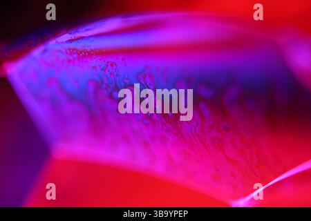 Red and purple fluid reflections on black background, liquid surface abstraction, colour edge, deep dark backgrounds, geometric water shapes Stock Photo