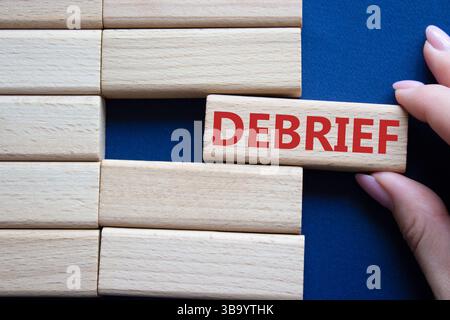Debrief symbol. Concept word Debrief on wooden blocks. Businessman hand. Beautiful deep blue background. Business and Debrief concept. Copy space. Stock Photo
