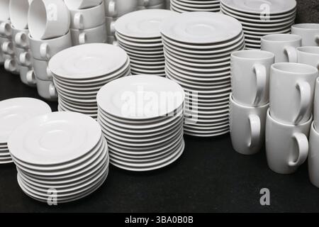 Stacked white tableware set. Plates cups and saucers. Clean porcelain dishes. Catering equipment ready. Minimal kitchen background. Elegant restaurant Stock Photo