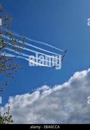Air show with five airplanes flying in formation with white smoke trails curving upward through a bright blue sky scattered with fluffy clouds Stock Photo
