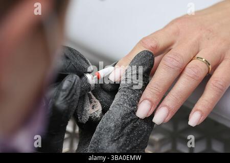 Nail care with drill tool. Electric manicure treatment. Hands in beauty gloves. Professional nail technician work. Precise grooming for healthy hands. Stock Photo