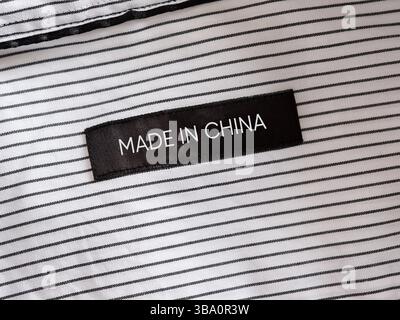 Black clothes label with the word made in China stitched on a white and black striped shirt. Chinese textile manufacturing. Stock Photo