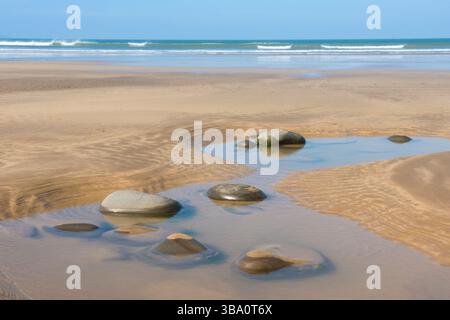 artistic creative picture of large stones in a pool on a sandy beach with waves breaking on the horizon under a blue sky, Westward Ho! Devon Stock Photo