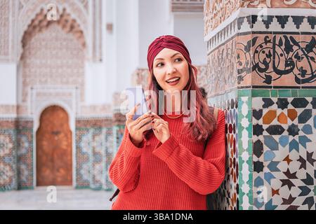 Young woman using mobile phone in front of mosaic wall, enjoying Moroccan travel experience Stock Photo