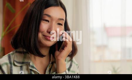 Happy Asian Korean woman talking client mobile phone female freelance writing notes businesswoman work home cellphone write information smiling girl Stock Photo