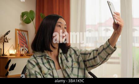 Asian Korean Chinese Japanese woman holding using mobile phone smartphone female girl make photo picture selfie web camera posing blogger influencer Stock Photo