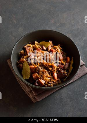 Traditional polish Bigos in bowl on dark stone background. Stewed cabbage with sauerkraut, mushrooms, smoked meats and spices. Close up view Stock Photo