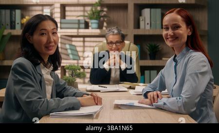 Three multiracial happy females business team businesswomen coworkers office girls group colleagues portrait Caucasian Asian women smiling posing Stock Photo