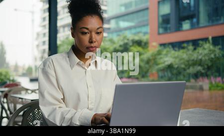 African American woman laptop computer web freelance typing work job manager employee entrepreneur online internet female girl businesswoman city cafe Stock Photo