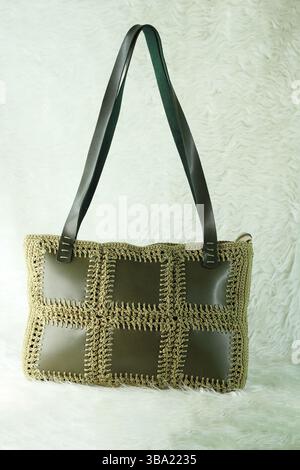 Green shoulder bag knitted using faux leather pieces on a white fluffy blanket. Close-up. Bag crocheted with square motifs. Stock Photo