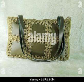 Green shoulder bag knitted using faux leather pieces on a white fluffy blanket. Close-up. Bag crocheted with square motifs. Stock Photo