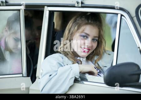 A girl with bright makeup looks out of the window of a retro car Stock Photo