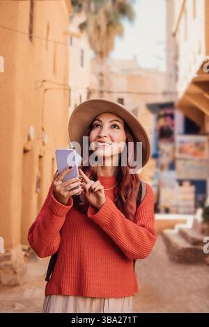 Young woman tourist using smartphone app and smiling while visiting Marrakech medina in Morocco Stock Photo
