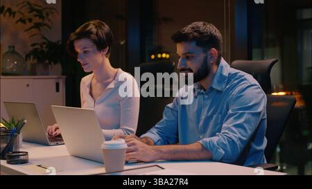 Professional team co-workers multiracial business man woman in dark night office typing laptops Indian businessman Caucasian businesswoman computer Stock Photo