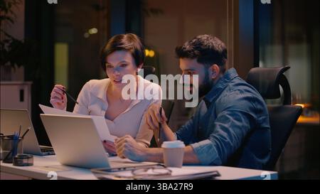 Multiracial teamwork Indian man Caucasian woman business partners co-workers colleagues talking at dark night evening office girl guy businessman Stock Photo