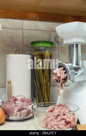 Home electric meat-grinder is making pork stuffing in a modern kitchen. Pork stuffing in a glass bowl Stock Photo