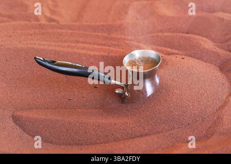 Coffee prepared on street in traditional Arabic way, cezve or ibrik small Turkish coffe pot is placed in red hot sand until liquid boils, closeup deta Stock Photo