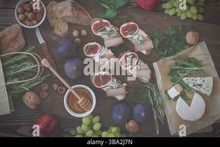 Sandwiches with ricotta, fresh figs, prosciutto, rosemary and blue cheese, walnuts and honey on rustic wooden board over black backdrop, top view. Del Stock Photo