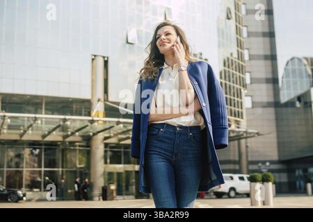 Caucasian business woman speaking by phone. Waist up portrait of a successful European business woman woman, talking on the phone, standing on glass b Stock Photo