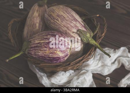 Purple graffiti eggplants in a wicker basket in a vintage wooden background in rustic style, selective focus Stock Photo