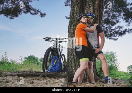 Happy couple with mountain bike sit embracing leisure nature outdoors. happy couple, lead an active lifestyle, stopped in woods near tree take a break Stock Photo