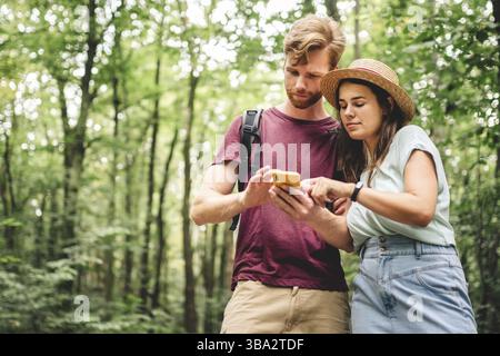 Young caucasian couple uses a smartphone to navigate in the forest. Hiking tourists orientation on the terrain using an online map, an application in Stock Photo