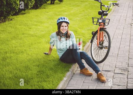 Subject ecological mode of transport bicycle. Beautiful young Caucasian woman wearing a blue helmet and long hair poses standing next to an orange-col Stock Photo