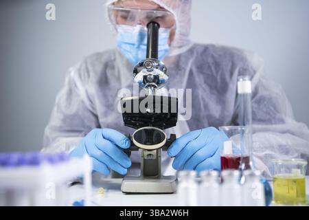 Scientist examining sample with a microscope, doing medical research in science laboratory. Male laboratory assistant in protective clothing studying Stock Photo
