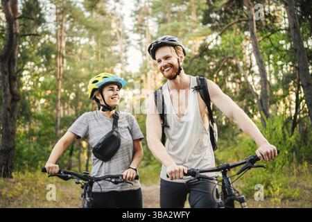Gorgeous couple riding on bikes in park forest. Romantic trip by bicycles. Active weekend. Sport couple. Man and woman cyclists. Eco friendly transpor Stock Photo