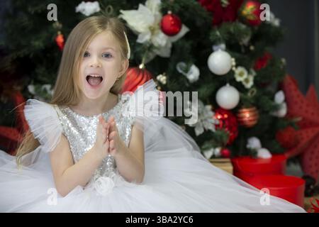 Beautiful child with a christmas gift. Dressing up girl at the New Year tree Stock Photo