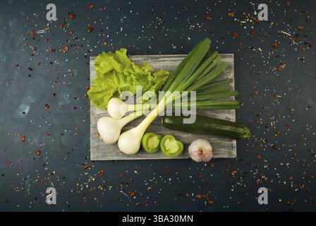 FRESH VEGETABLES AND SPICES ON A WOODEN BOARD ON A DARK STONE BACKGROUND. THE CONCEPT OF VINTAGE. SPICES THE YOUNG CORN ASPARAGUS GREEN TOMATO CUCUMBE Stock Photo