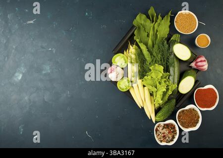THE VEGETABLES IN THE BOX ON THE STONE A DARK BACKGROUND. YOUNG GREENS ONION GARLIC ZUCCHINI BRIGHT SPICES LAY IN A WOODEN TRAY WITH HANDLES ON A DARK Stock Photo