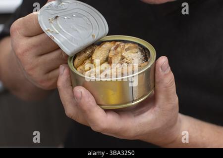Hands open a metal fish can with sprats Stock Photo
