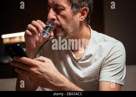 Man drinking vodka and using mobile phone, selective focus Stock Photo