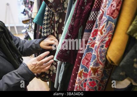 Senior woman going through clothes in second hand thrift charity shop, detail on her moving hands, London, United Kingdom, Europe Stock Photo