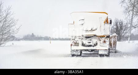 Orange plough truck on snow covered road, gray sky and trees in background, view from back - winter road maintenance, Podbanske, Slovakia, Europe Stock Photo