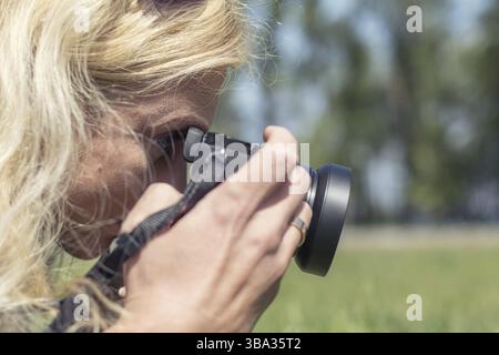 Professional woman photographer taking outdoor with prime lens, during a sunny day in the spring park. Shallow depth of field. Toned Stock Photo