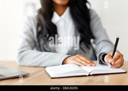 Unrecognizable black female secretary writing down info during online business meeting at workplace, selective focus Stock Photo