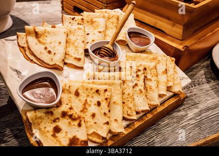 Thin pancakes served on white marble tray on wooden table with chocolate cream and honey ready for breakfast Stock Photo