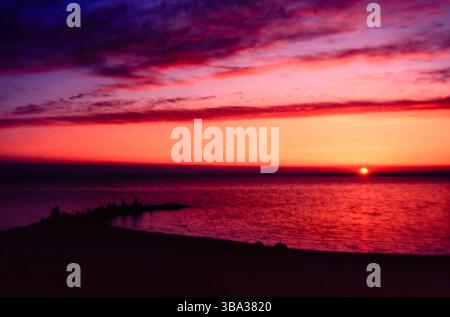 Yellow setting sun at a cove  over Lake Huron under a red and purple sky with the foreground in darkness. Stock Photo