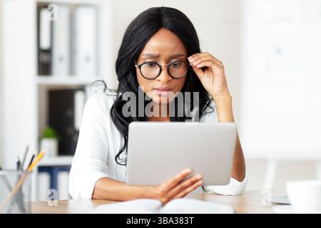 Serious female entrepreneur working on tablet pc at office, participating in webinar or online conference at office Stock Photo