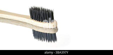 Wooden bamboo toothbrush with black bristles, closeup detail isolated on glossy white table reflection visible, space for text right side, Liptovsky H Stock Photo