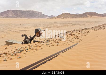 Old rusty unused railroad switch at Wadi Rum train station, tracks covered with sand near, desert and mountains in background Stock Photo