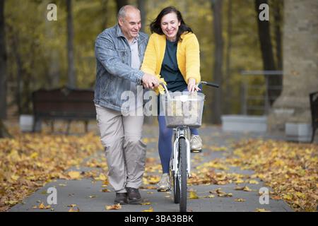 Happy middle aged couple with bike in autumn park. Elderly cheerful husband and wife on a walk Stock Photo