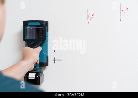 A man worker detecting hidden studs and rebars positions by a digital wall scanner on a white wall during home renovation Stock Photo