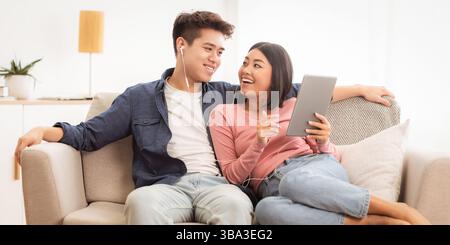 Japanese Spouses Using Tablet Browsing Internet Sitting On Couch Indoor Stock Photo