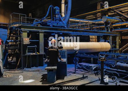 Factory engineer operates pipe painting automatic machine. Stock Photo