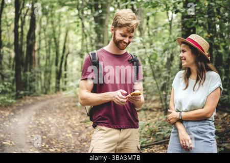 Hikers using mobile gps for directions. Happy couple checking smartphone in the woods during backpacking trip. Young joyful couple using gps map, navi Stock Photo