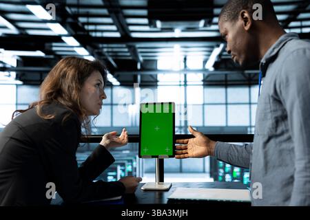 Programmers in data center brainstorming, using mockup tablet, observing analytics, reviewing equipment health. Team of server hub IT specialist use isolated screen device, adjusting system parameters Stock Photo