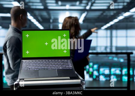 Isolated screen mockup laptop in front of technicians in blurry background supervising server room gear. Close up of chroma key notebook next to admins overseeing data center rigs Stock Photo